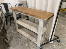 Load image into Gallery viewer, A narrow farmhouse-style bookcase or console table with a distressed white base and an Early American brown top, featuring a wooden shelving unit on one side.