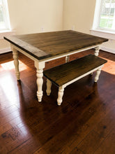 Load image into Gallery viewer, Angled view of farmhouse dining table and bench with dark walnut plank tops and antique-white legs near two windows
